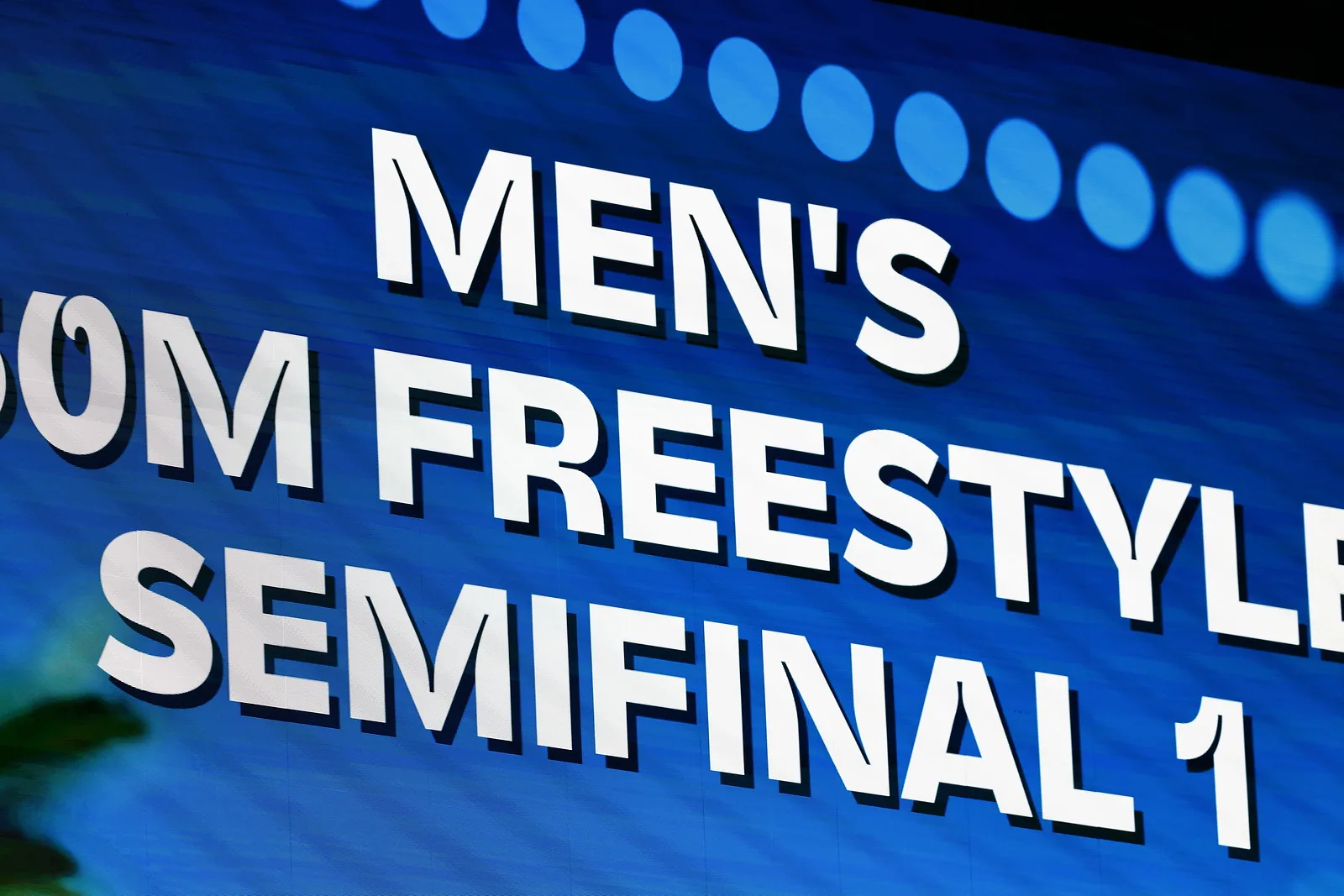 A venue screen displaying the words Men’s Freestyle Semifinal 1 in large white letters on blue.