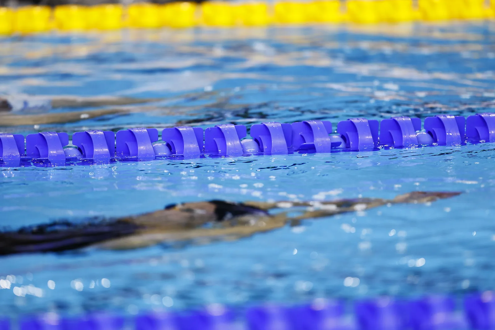 Close-up of pool lane ropes with a swimmer’s blurred form moving underwater behind them.