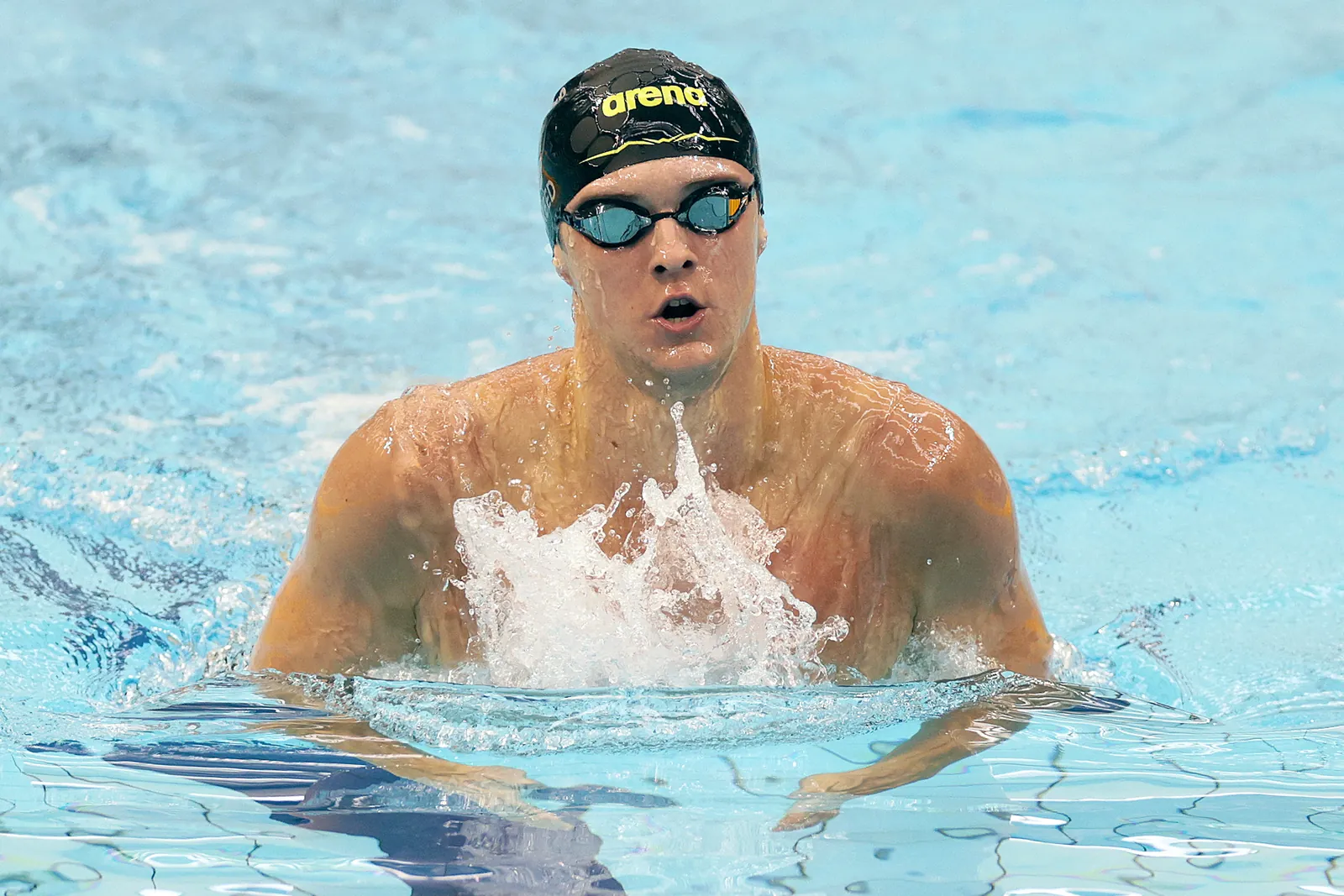 A swimmer rising to breathe mid-breaststroke, water sweeping off the shoulders.