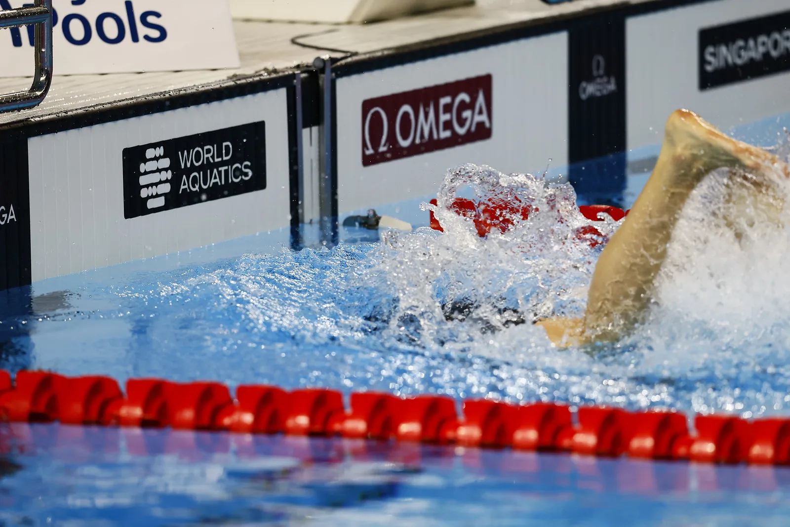 Close-up of a swimmer’s feet and legs throwing up spray beside the touch pads at the pool edge.