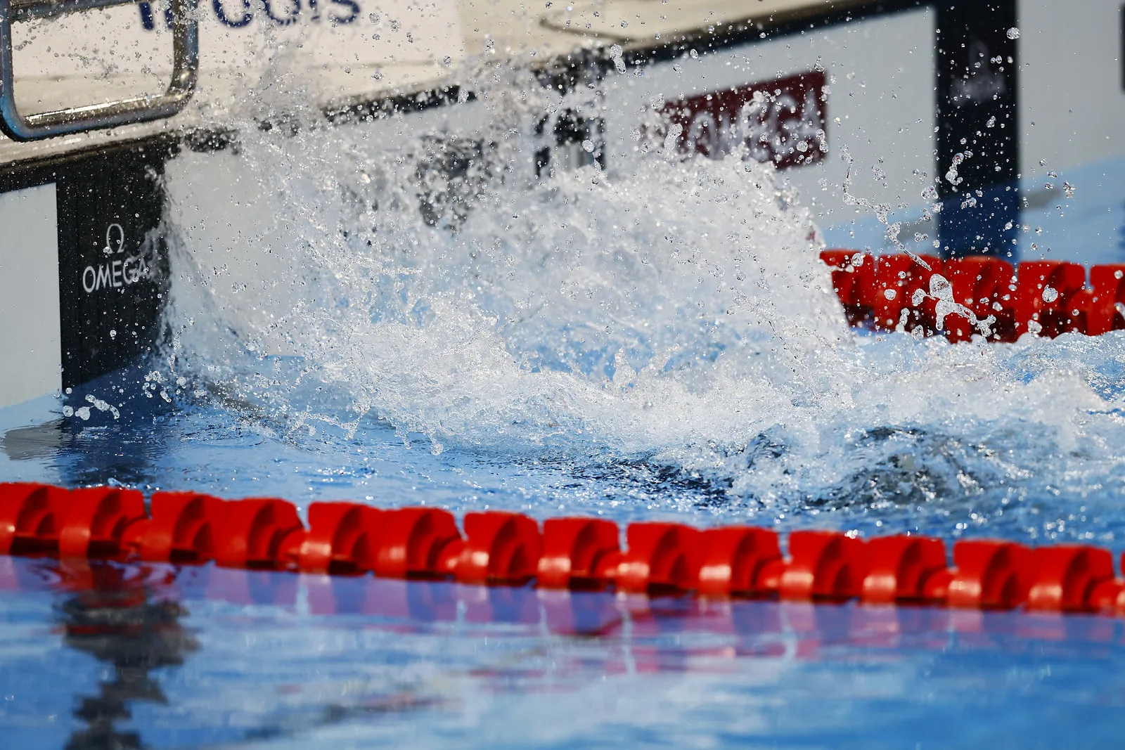 A large splash between red lane ropes at the edge of a competition pool.