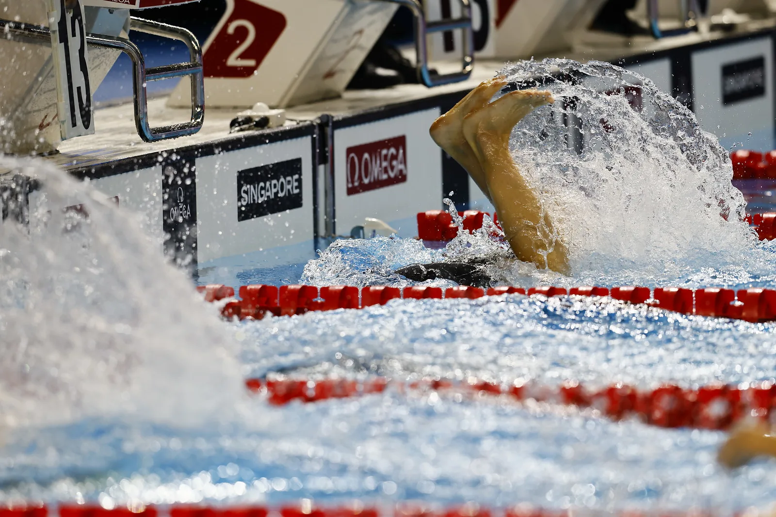 A swimmer performing a flip turn at the wall, feet emerging from a large splash.